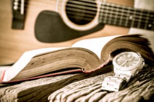 Watch and guitar with open book on old wooden table, vintage style.